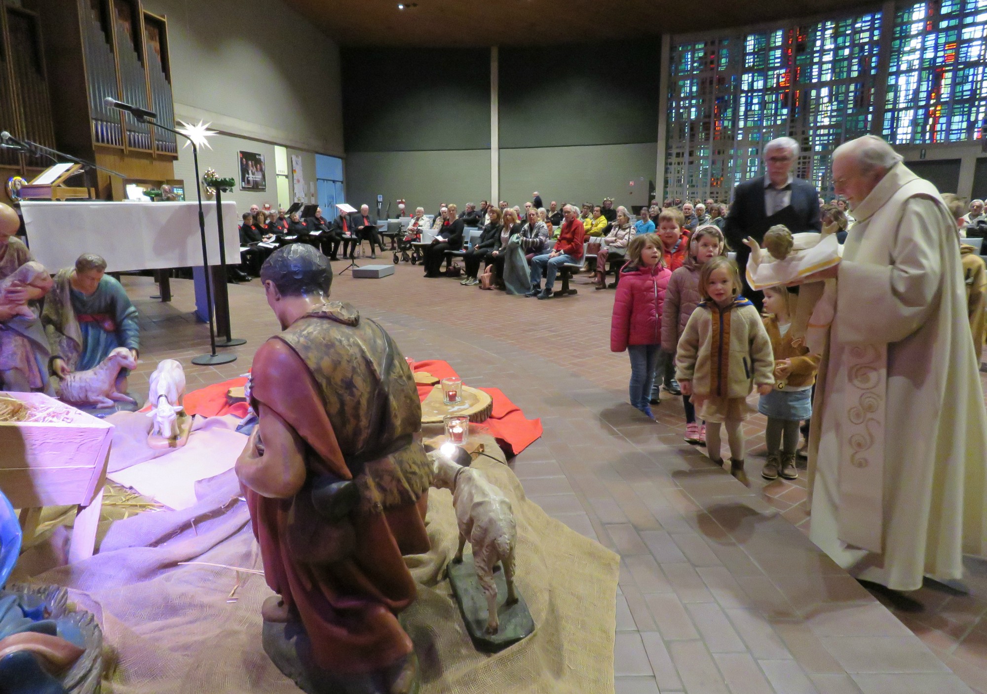 Priester Paul Scheelen legt het Kindje samen met andere kinderen in de kribbe van de kerststal